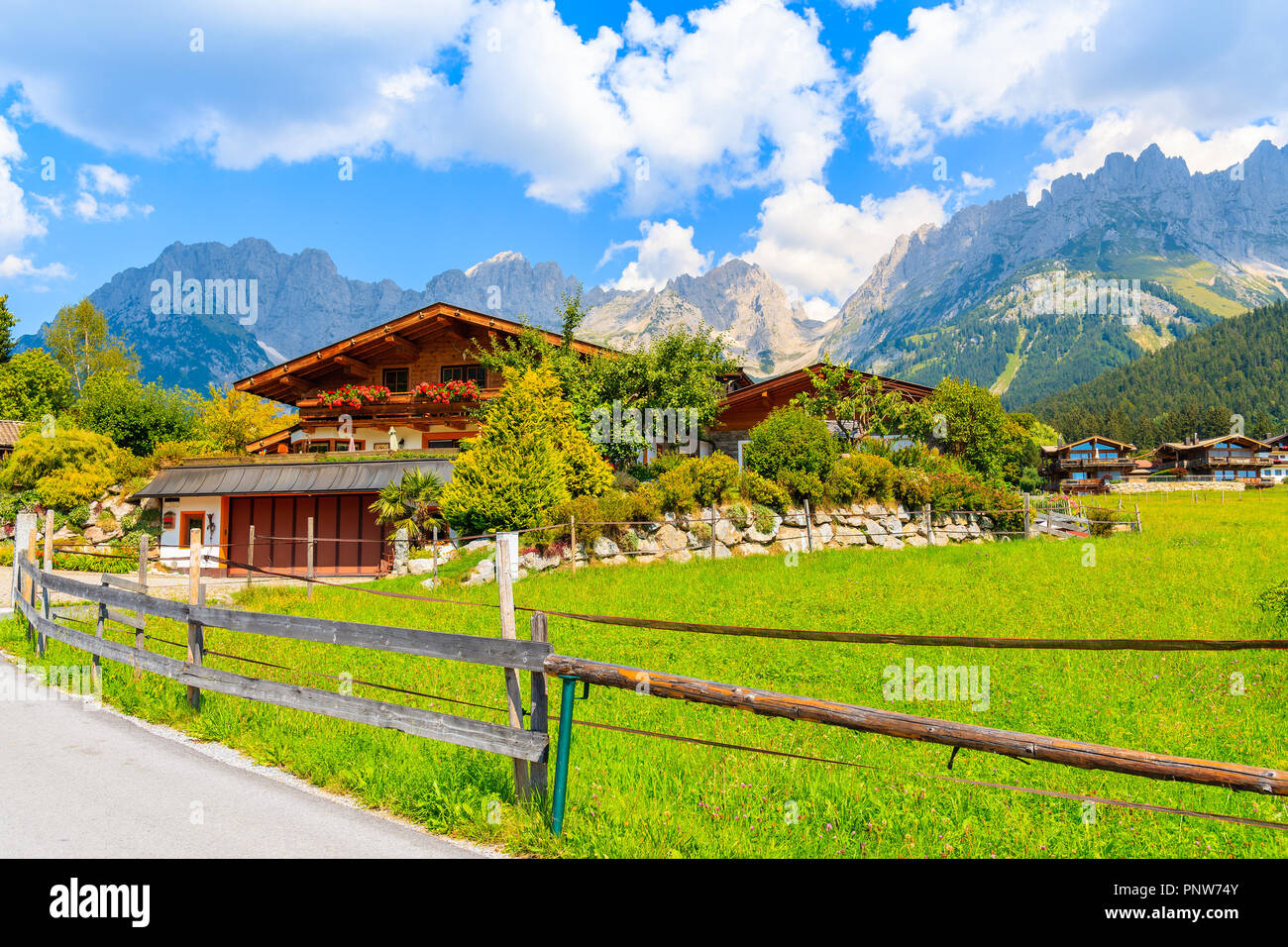 In legno tipico casa alpina contro Alpi montagne sullo sfondo verde prato a Going am Wilden Kaiser villaggio sulla soleggiata giornata estiva, Tirolo, Austria Foto Stock