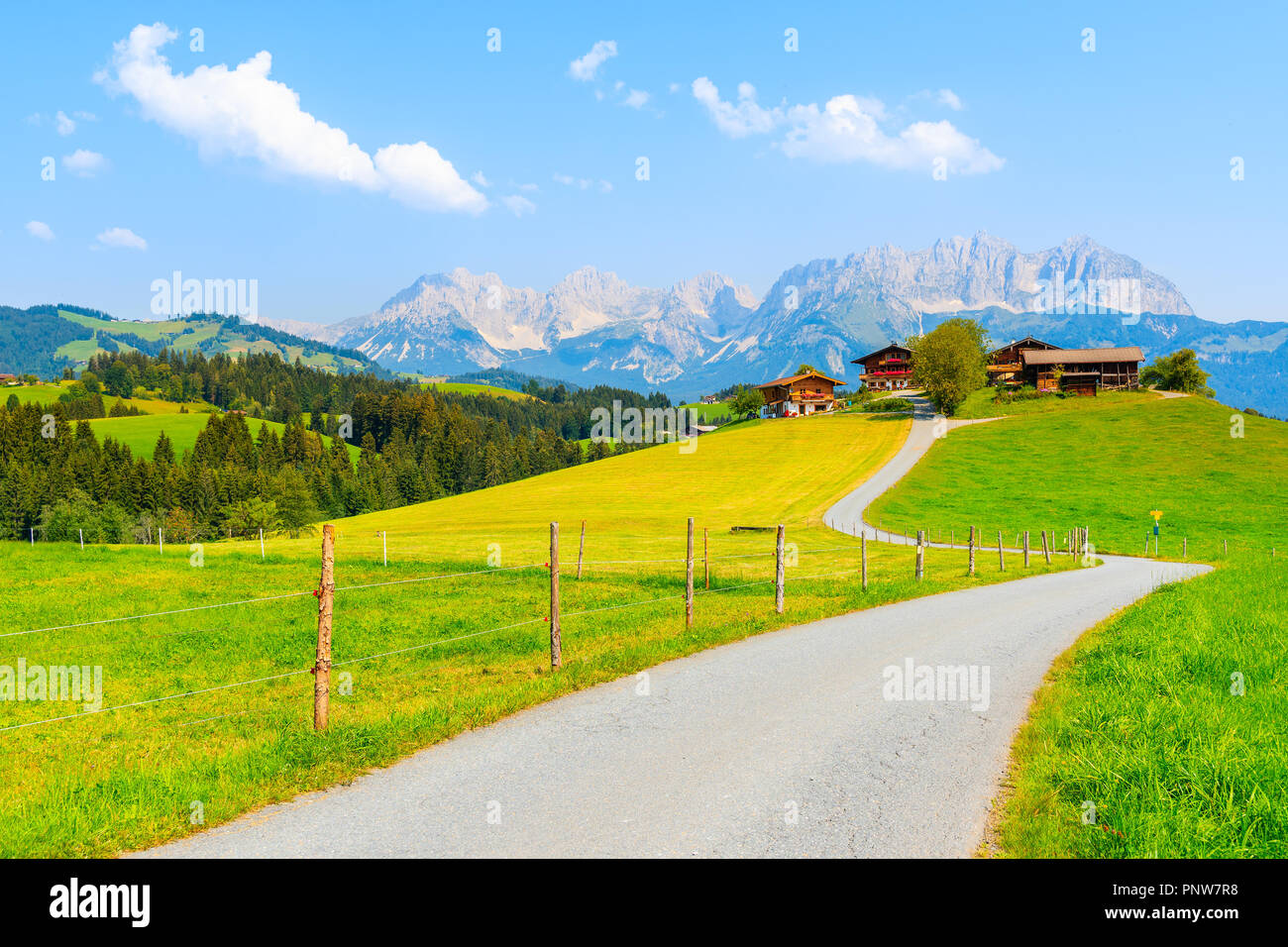 Strada lungo il verde prato in Gieringer Weiher zona di montagna che conduce alle tipiche case alpine sulla collina, Alpi Kitzbühel, Austria Foto Stock