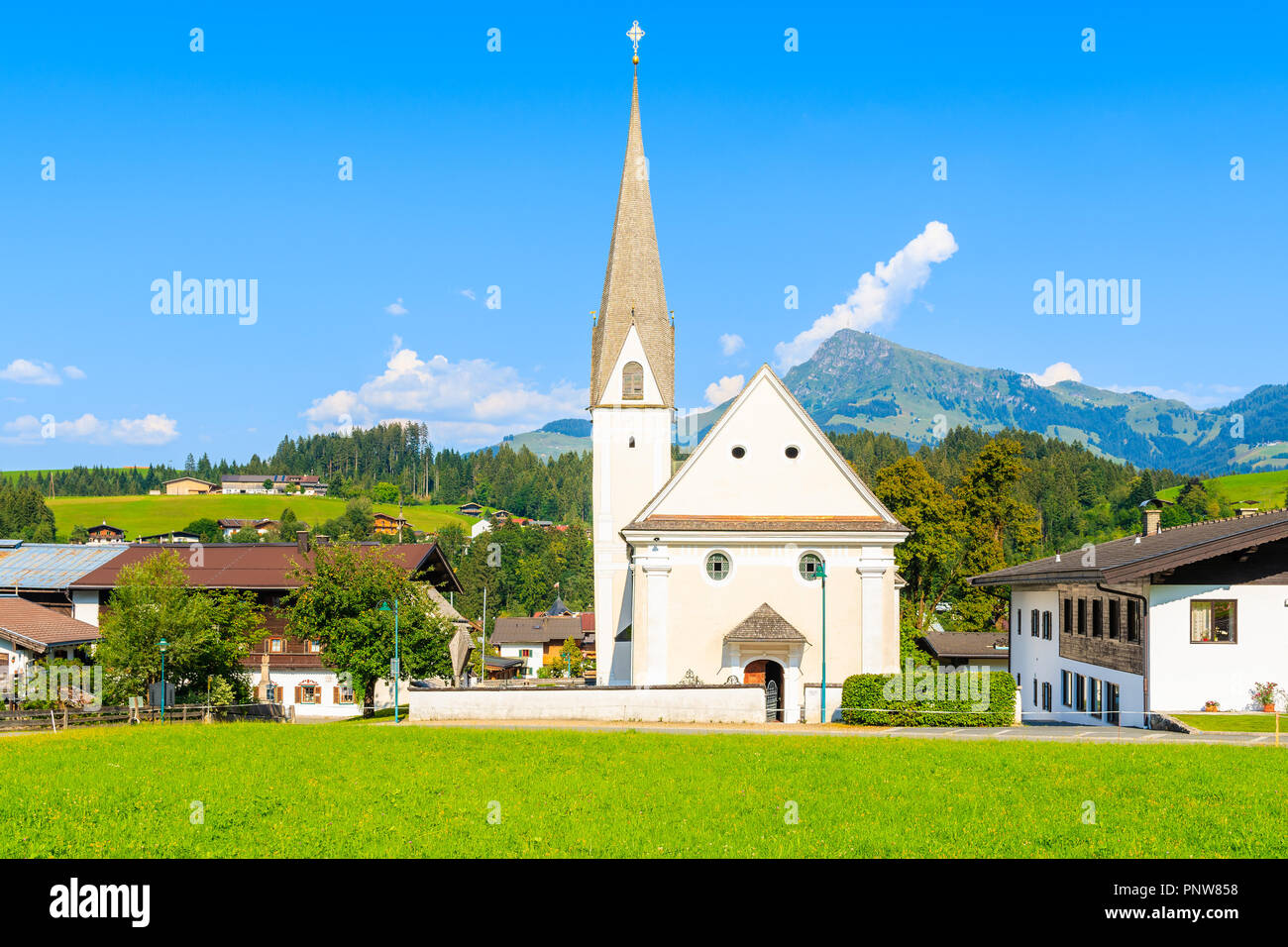 Tipica chiesa alpina contro Alpi montagne sullo sfondo verde prato in Reith bei Kitzbuhel villaggio sulla soleggiata giornata estiva, Tirolo, Austria Foto Stock
