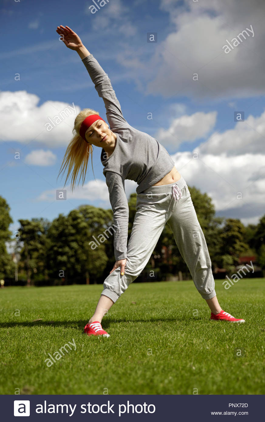 Donna bionda in una tuta di eseguire esercizi di stiramento nel parco Foto Stock