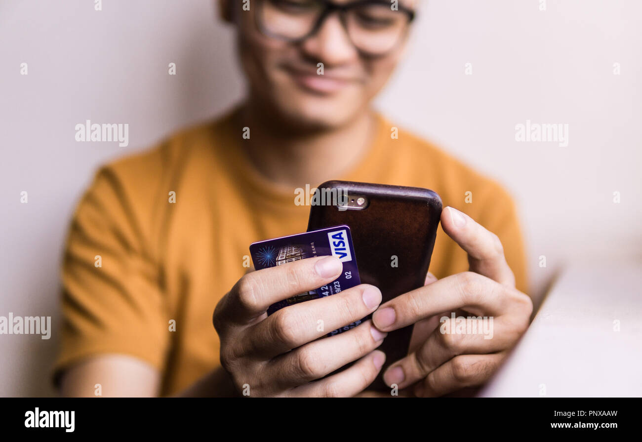 La mano di una persona in possesso di un telefono cellulare e una carta di credito per shoping on-line Foto Stock