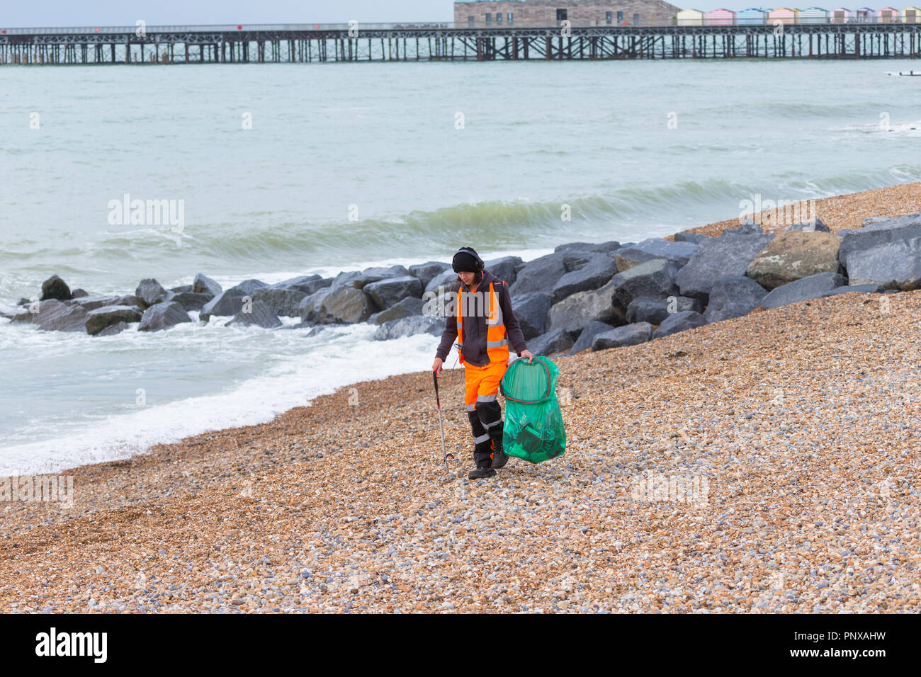 Giovane Uomo con cuffie di prelevare i rifiuti e la pulizia della spiaggia vestito in arancione Kier Azienda di abbigliamento, Hastings, east sussex, Regno Unito Foto Stock