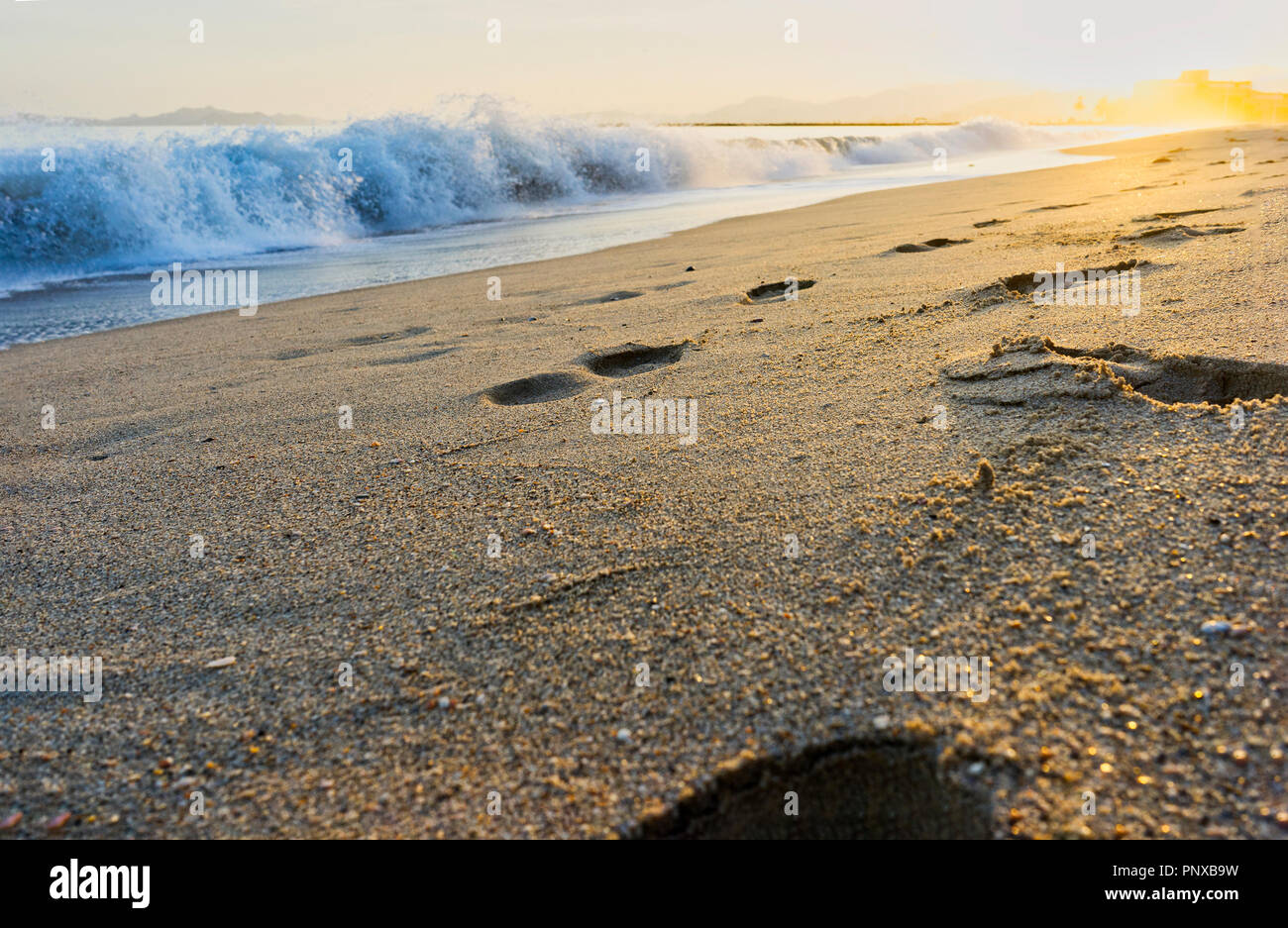 Orme nella sabbia e le onde che esplodevano in sabbia con numerosi schizzi. immagine per reprensentar energia e vacanze di tranquillità e di riflessione Foto Stock