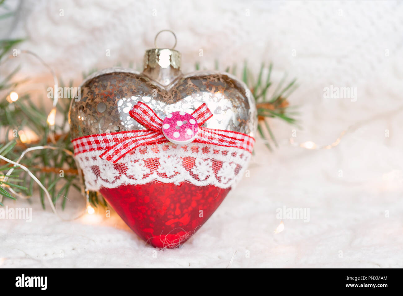 Giocattolo di Natale cuore su un bianco maglia maglione caldo circondato da ghirlande. Foto Stock