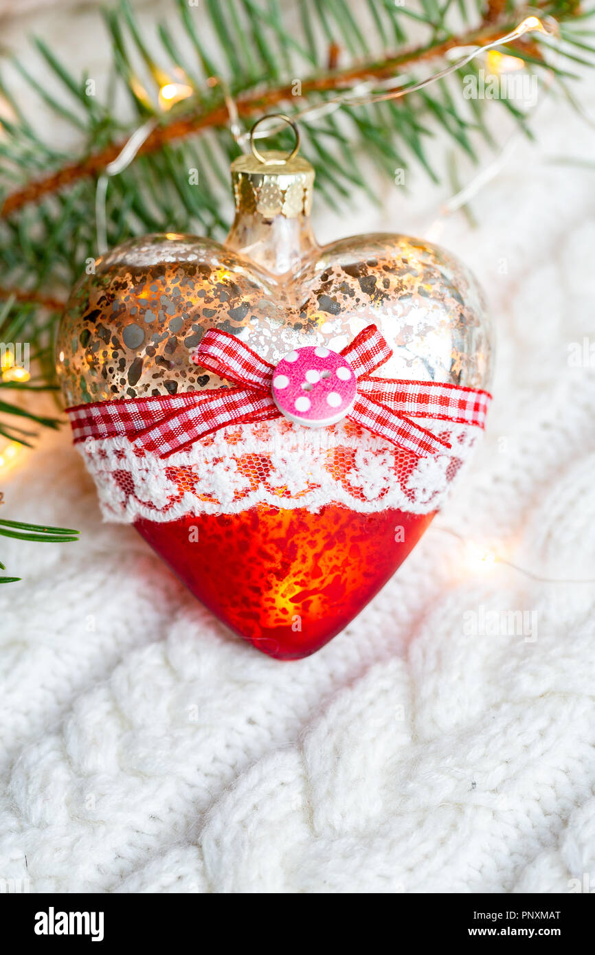 Giocattolo di Natale cuore su un bianco maglia maglione caldo circondato da ghirlande. In verticale Foto Stock