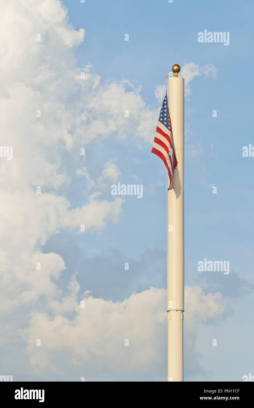 Una bandiera americana appesa alla sommità di un palo con una torreggiante, ragged cumulus cloud e il cielo azzurro in background. Foto Stock