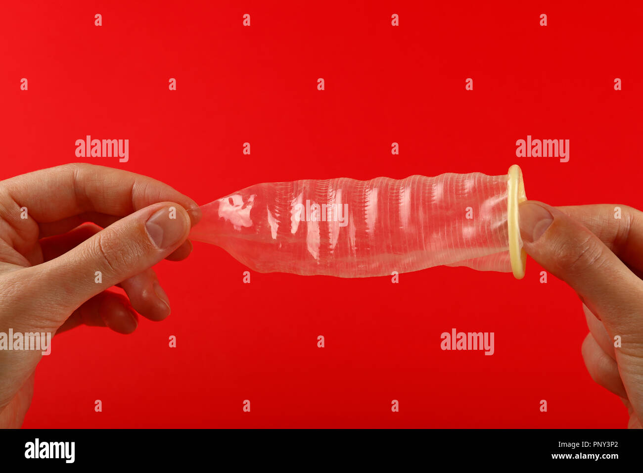 Vicino a due a due mani donna azienda uno aperto condom in lattice su sfondo rosso con copia spazio, basso angolo vista laterale Foto Stock