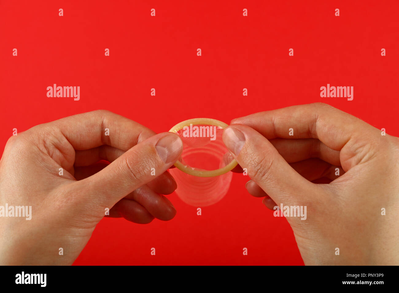 Vicino a due a due mani donna azienda uno aperto condom in lattice su sfondo rosso con copia spazio, basso angolo vista laterale Foto Stock