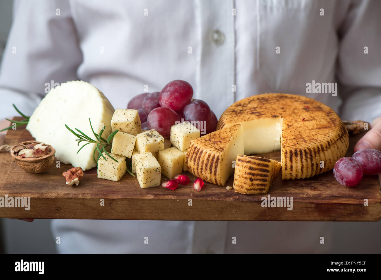 Un vassoio di formaggi con formaggi assortiti, uva, i dadi e le mani del casaro su sfondo nero. Formaggi italiani e piatti di frutta. Foto Stock