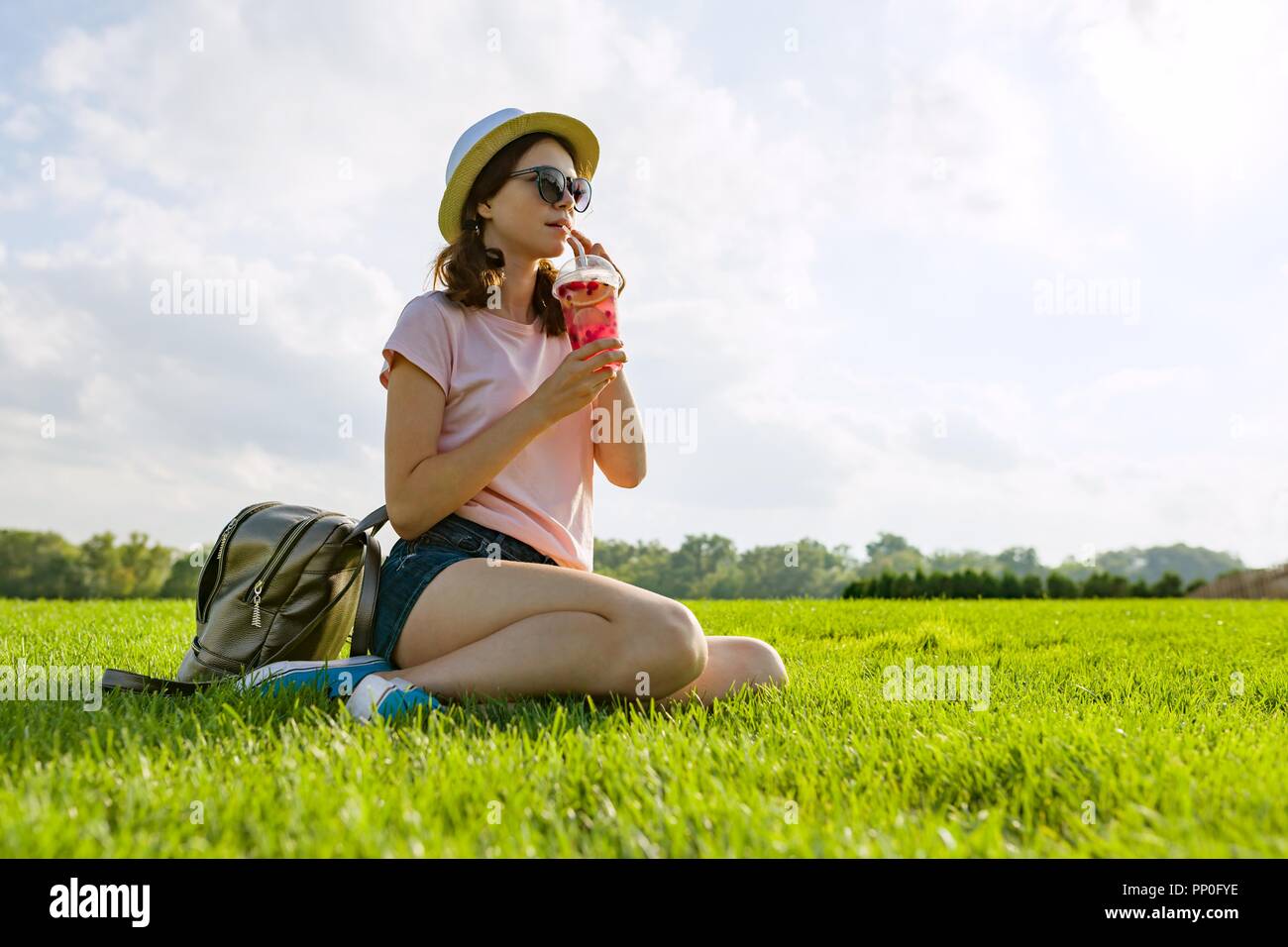 Giovane ragazza in occhiali da sole e cappello bevande estate berry drink  con ghiaccio seduti sul prato verde. Spazio di copia Foto stock - Alamy
