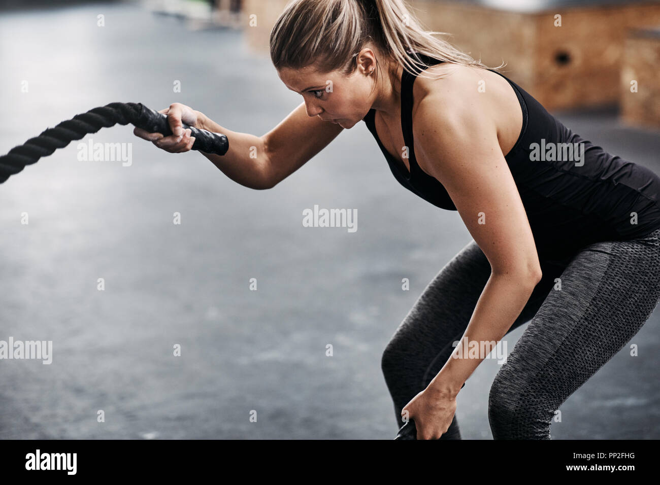 Montare la giovane donna abbigliamento sportivo in esercizio con funi durante una sessione di allenamento in palestra Foto Stock