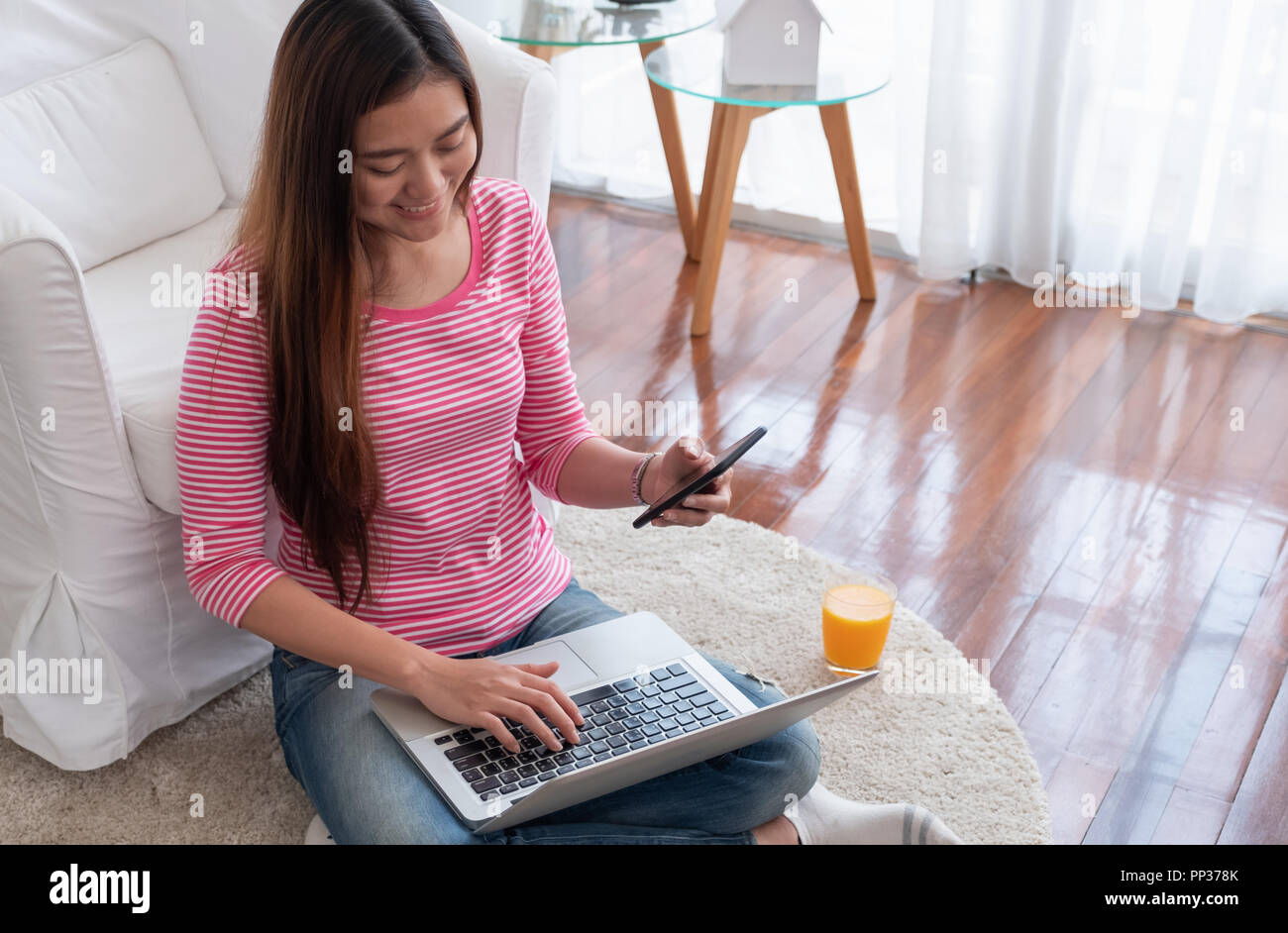 Femmina asiatica seduta sul pavimento utilizzare mobile con il computer portatile shopping online nel salotto di casa.Il lavoro a casa concetto.uno stile di vita digitale Foto Stock