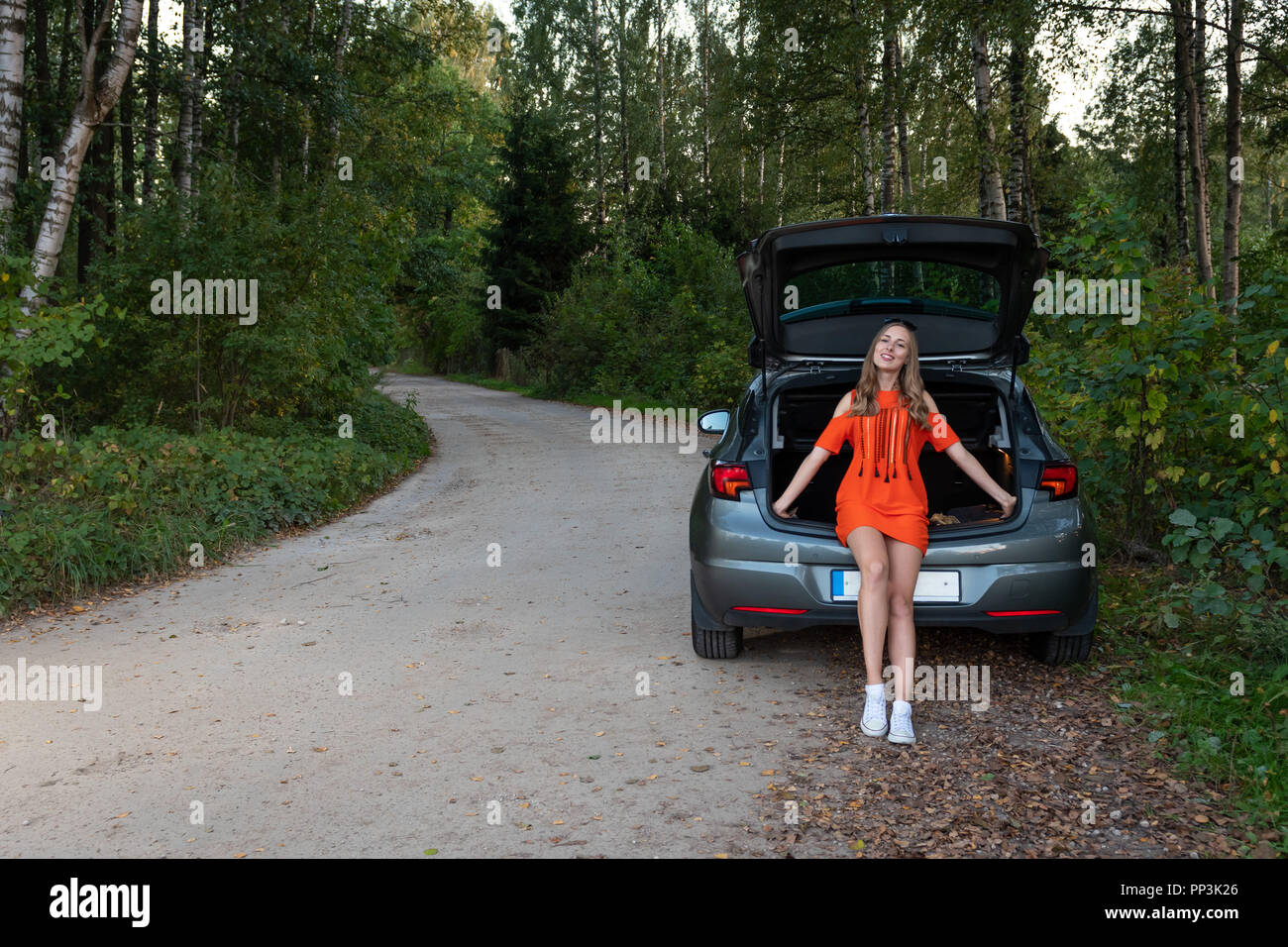 Un sorridente giovane donna a lato della strada, sedersi sul bordo delle auto del boot Foto Stock