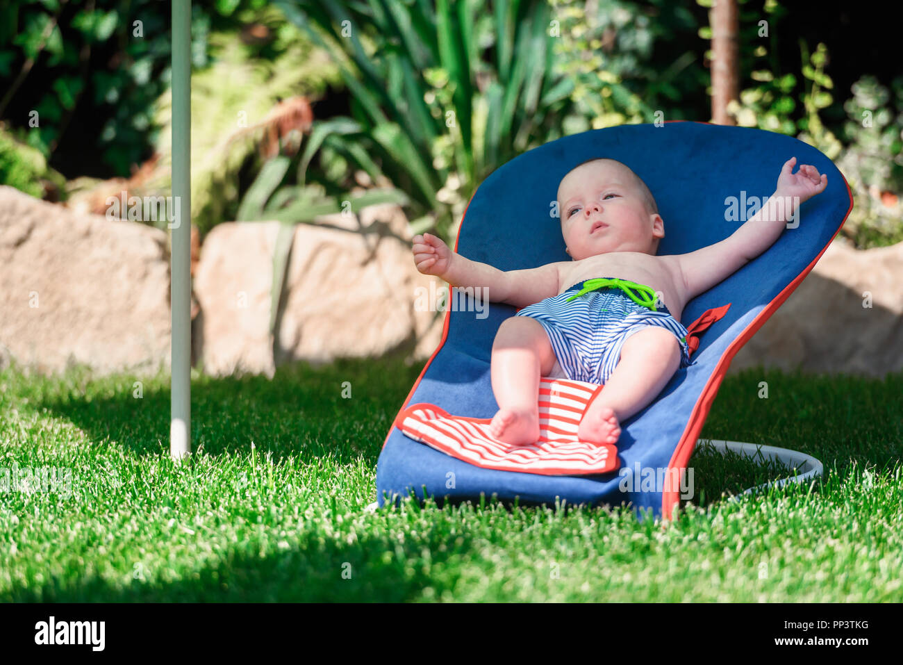 Baby boy si trova su una sedia a sdraio sul prato verde. Rilassatevi e concetto di vacanza Foto Stock