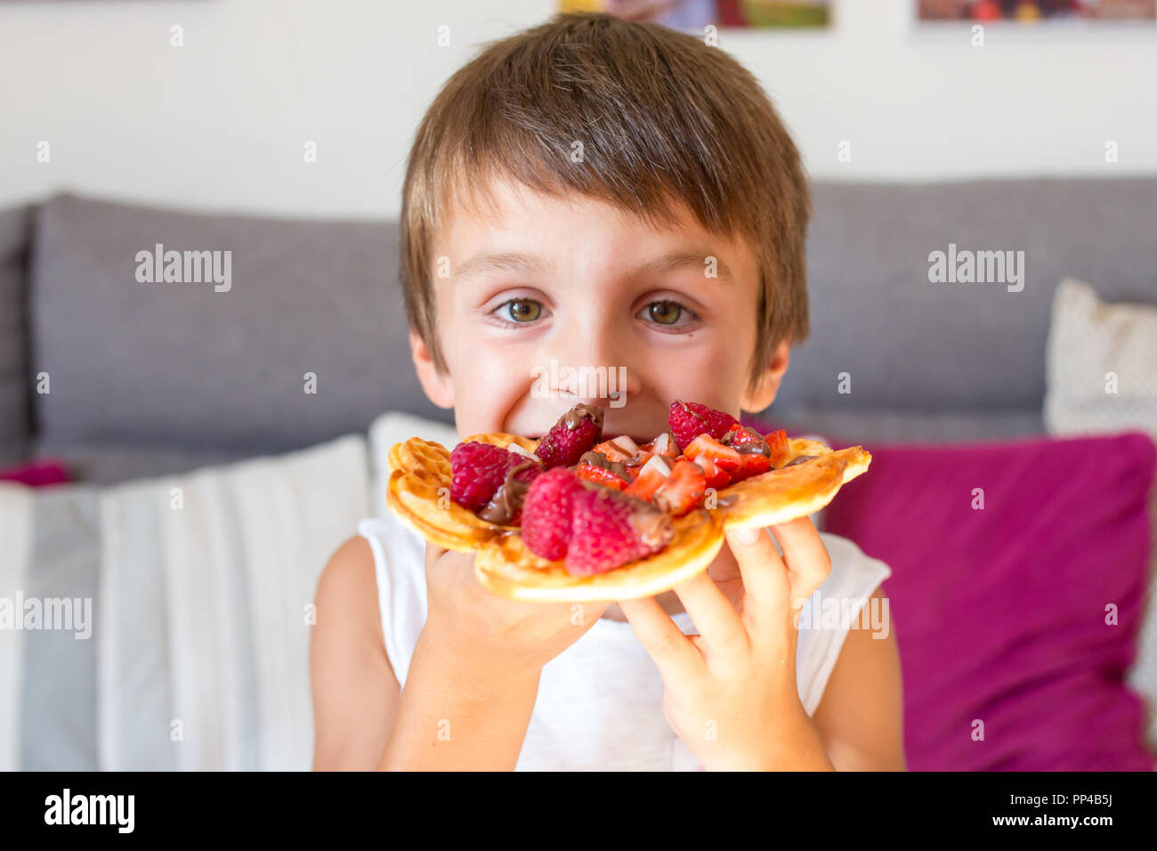 Dolce ragazzo di compleanno, mangiare i waffle belgi con fragole e lamponi e il cioccolato a casa Foto Stock