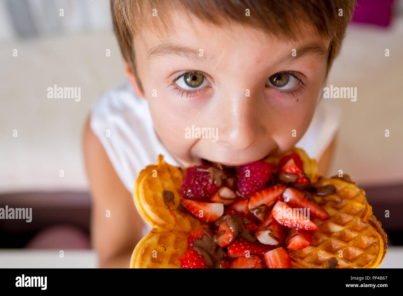 Dolce ragazzo di compleanno, mangiare i waffle belgi con fragole e lamponi e il cioccolato a casa Foto Stock