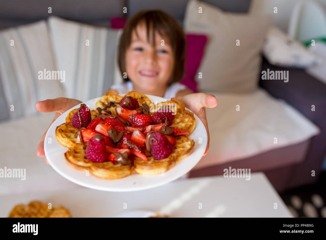 Dolce ragazzo di compleanno, mangiare i waffle belgi con fragole e lamponi e il cioccolato a casa Foto Stock