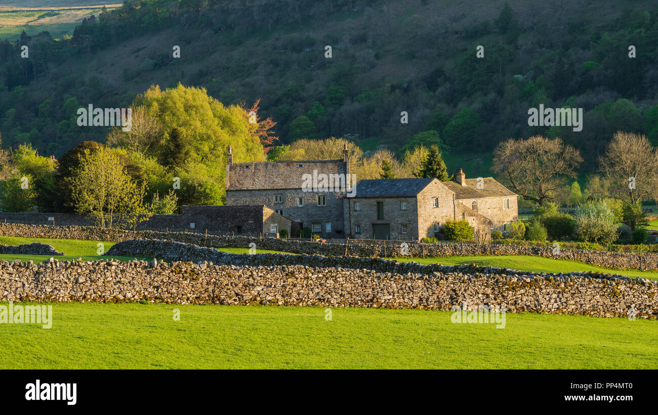 Storico, Stone Manor House & fabbricati agricoli, nella splendida e soleggiata campagna immerso sotto la ripida collina - Buckden, Yorkshire Dales, Inghilterra, Regno Unito. Foto Stock