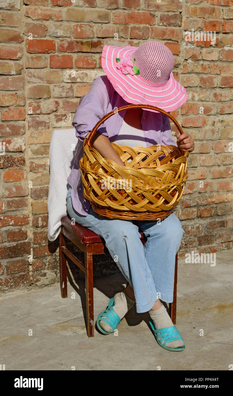 Close-up completa lunghezza ritratto di donna matura in largo-colmato il  cappello che è seduto sulla sedia piegando il capo più grande cesto in  vimini sulle ginocchia in Foto stock - Alamy
