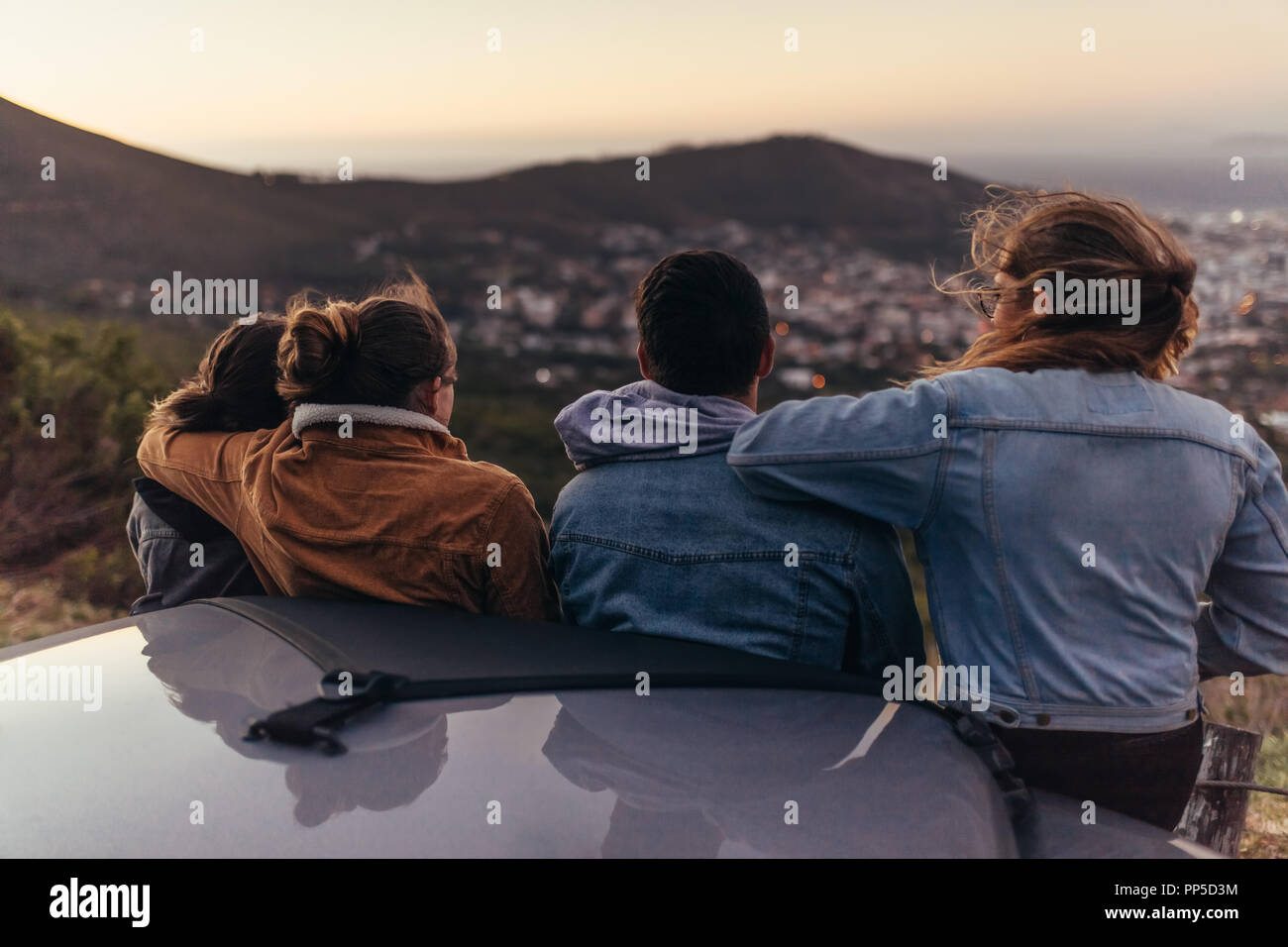 Vista posteriore di due coppie in piedi su un'autostrada. Gruppo di amici su un disco di arresto su una autostrada e guardando la città dalla cima di una collina. Foto Stock