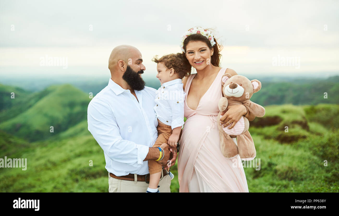 Famiglia di origine ispanica di tre piedi su una verde collina sullo sfondo Foto Stock