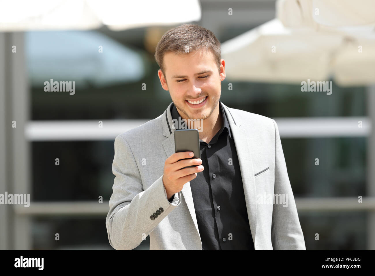 Vista anteriore verticale di un esecutivo a camminare verso la telecamera utilizzando uno smart phone in strada Foto Stock