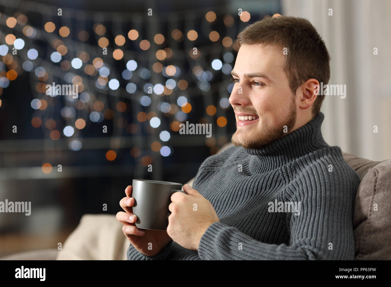 Uomo in possesso di una tazza da caffè guardando lontano nella notte seduto su un divano nel salotto di casa Foto Stock