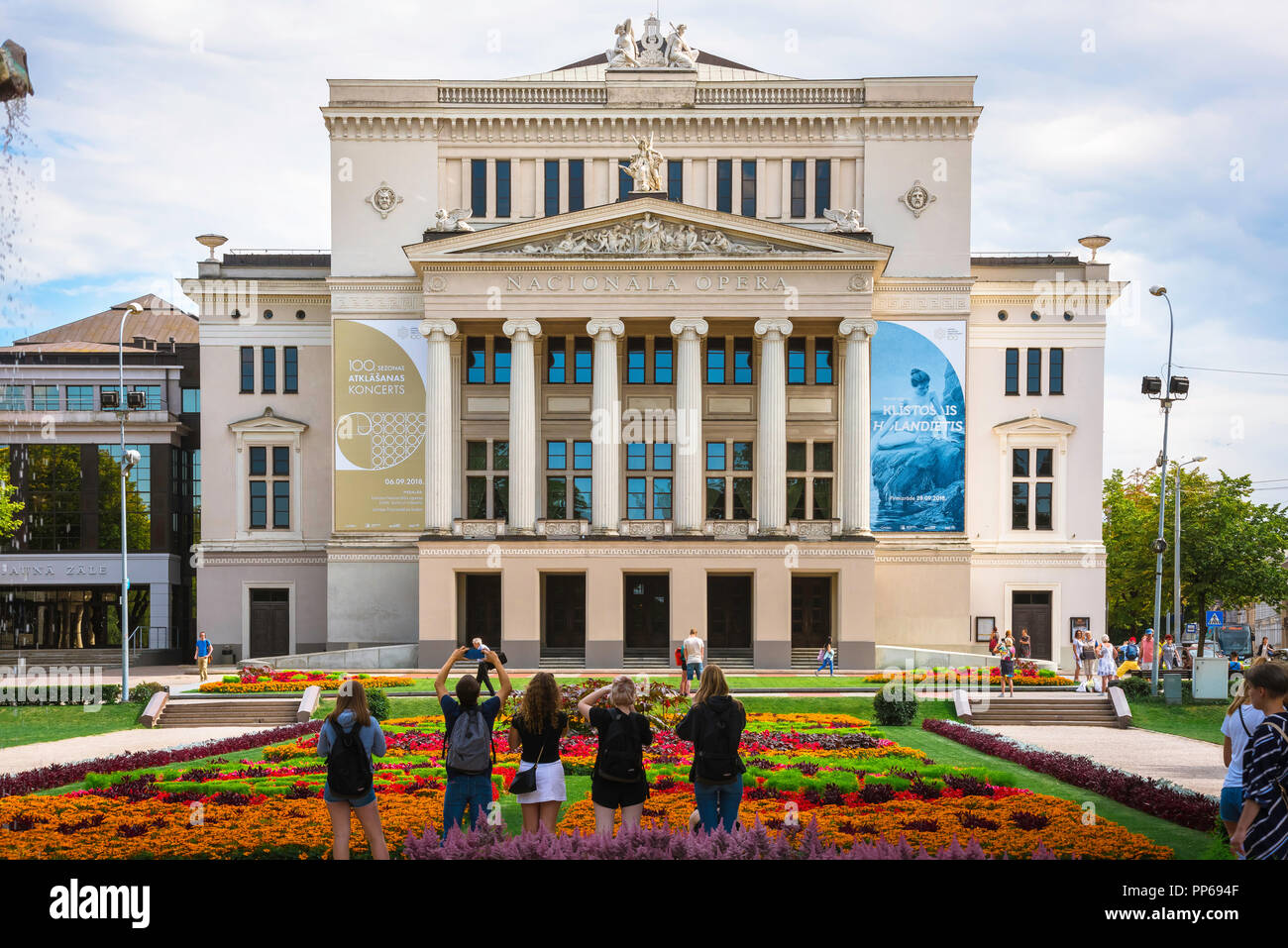 Teatro dell'Opera di Riga, vista posteriore dei turisti in Strulaka parco e giardino a fotografare il Riga Opera House Edificio con gli smartphone, Lettonia. Foto Stock