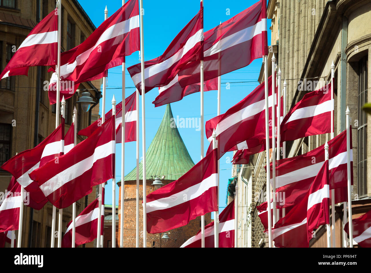 Lettonia colore, vista delle bandiere nazionali lettone in esposizione nel centro della città di riga con il tetto della Torre della polvere sullo sfondo, Lettonia. Foto Stock