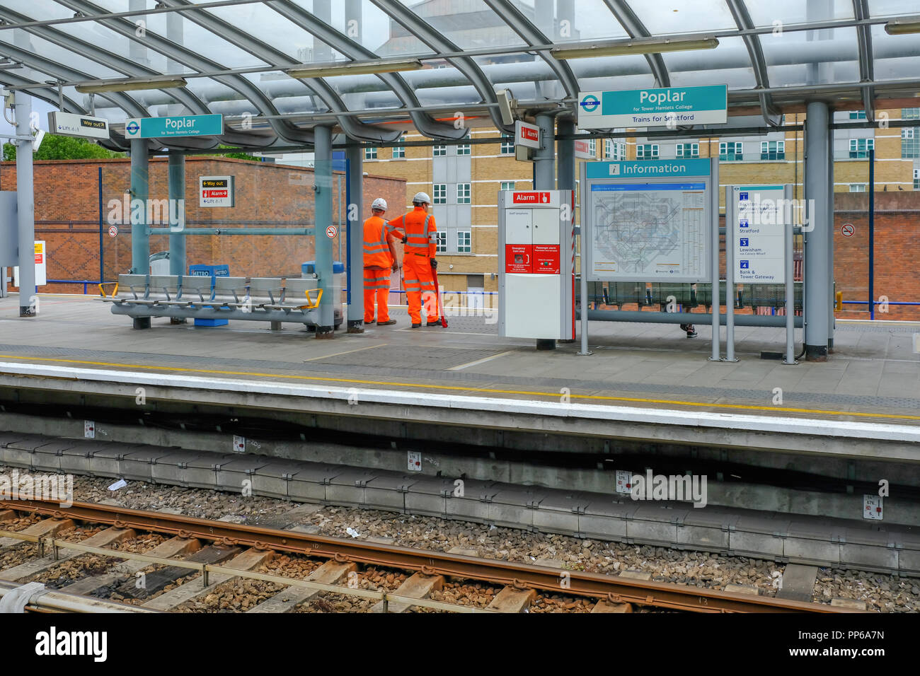 Il pioppo, London, Regno Unito - 18 agosto 2018: due operai vestiti di alta viz uniforme in arancione. Mostra la workment in attesa sulla piattaforma di DLR per un treno. Foto Stock