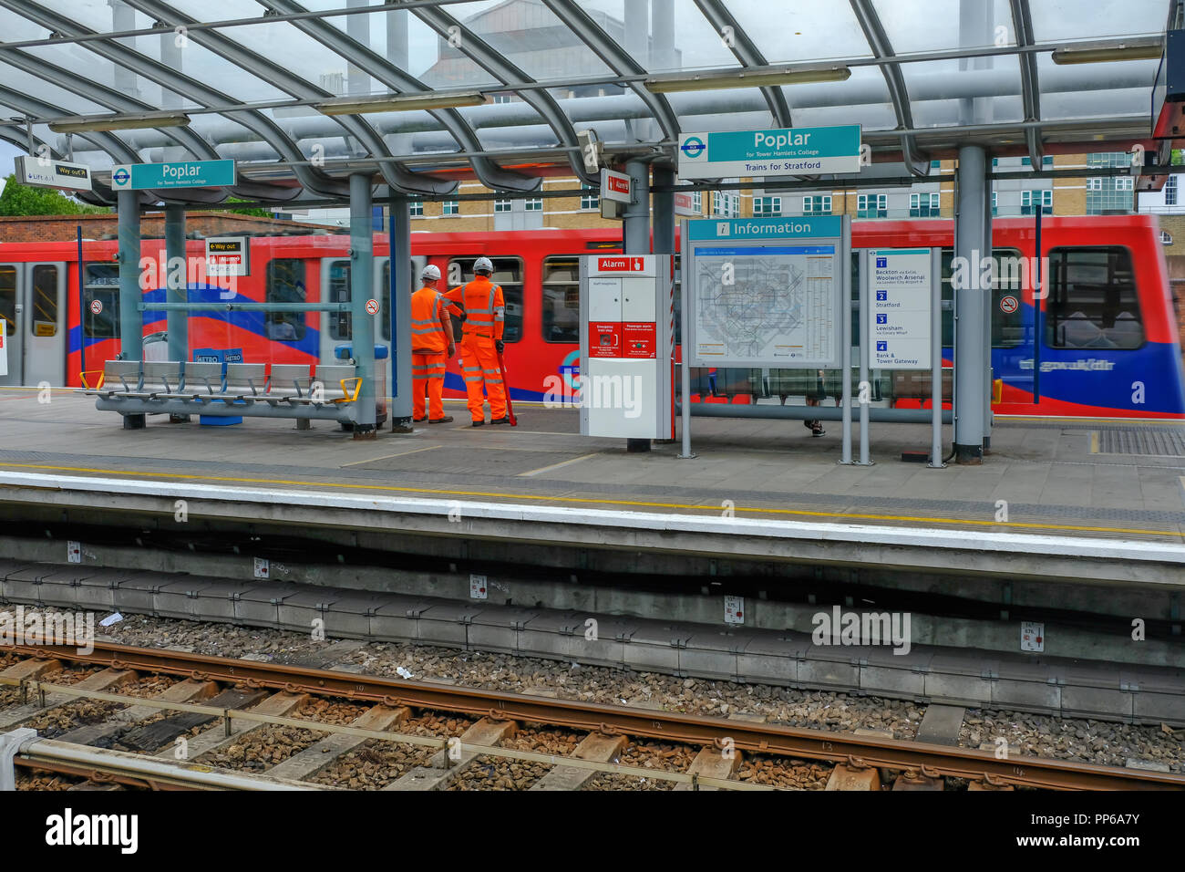 Il pioppo, London, Regno Unito - 18 agosto 2018: due operai vestiti di alta viz uniforme in arancione. Mostra la workment su DLR piattaforma come un treno tira a. Foto Stock