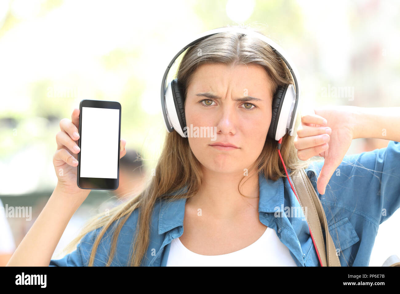 Vista anteriore verticale di un arrabbiato teen ascoltando la musica che mostra un telefono intelligente schermo in strada Foto Stock