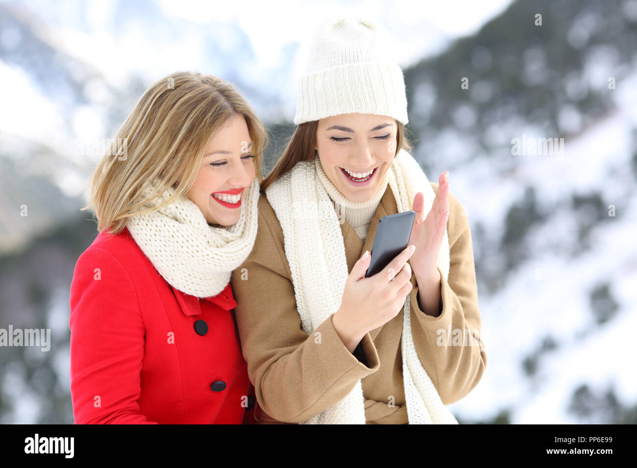 Due amici felice guardando il contenuto del telefono su vacanze invernali in una montagna innevata Foto Stock