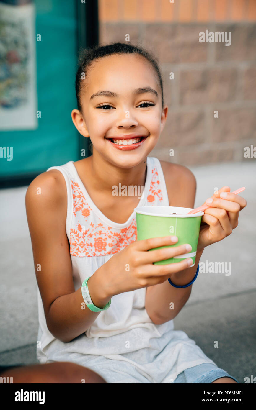 Sorridente ragazza seduta sui gradini a mangiare il gelato Foto Stock