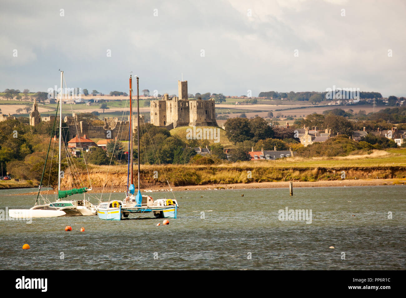 Il castello di Warkworth visto dal porto a camminare attraverso l'estuario e lungo il fiume Coquet con barca a vela e barche da pesca ormeggiate Northumberland England Regno Unito Foto Stock