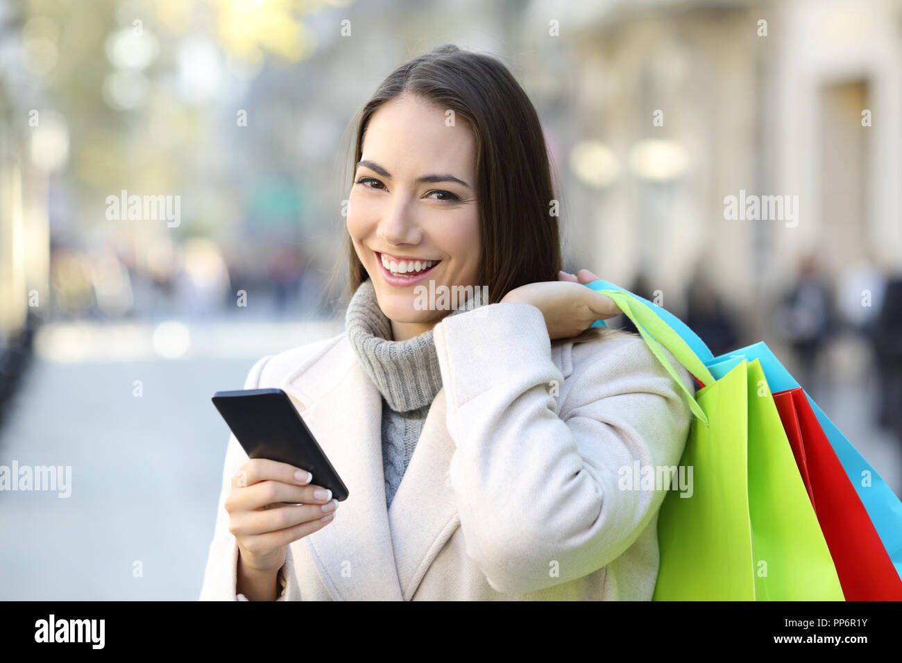 Happy shopper in possesso di una smart phone e colorate le borse della spesa in inverno in strada Foto Stock