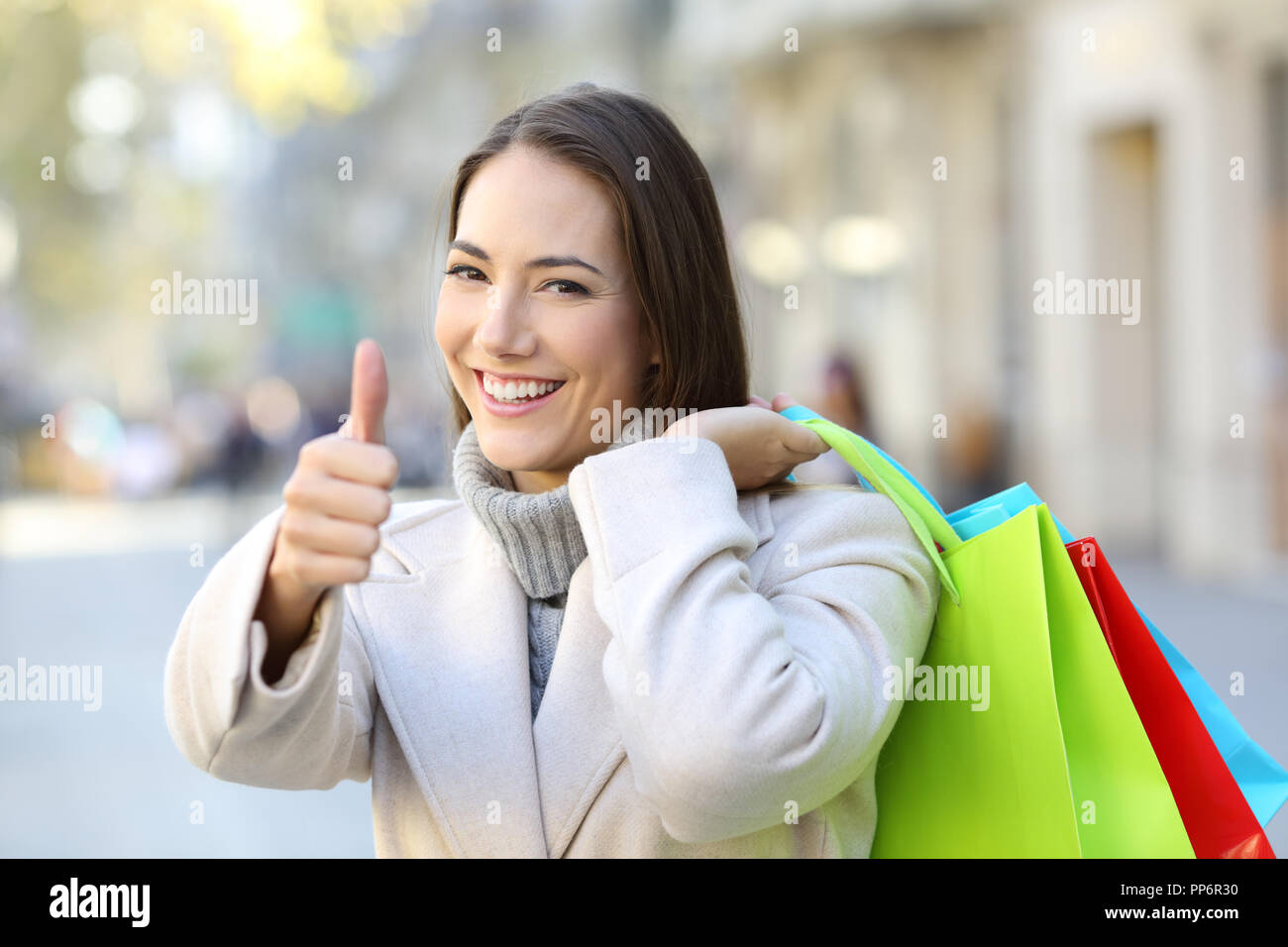 Happy shopper con pollice in alto tenendo le borse della spesa in inverno in strada Foto Stock