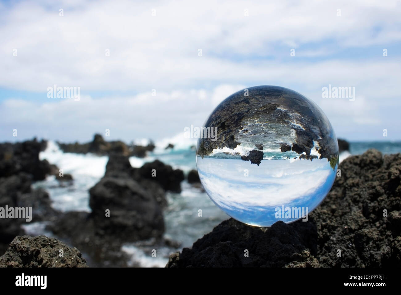 Costa di lava con rottura onde turchesi catturati nella sfera di vetro la riflessione Foto Stock