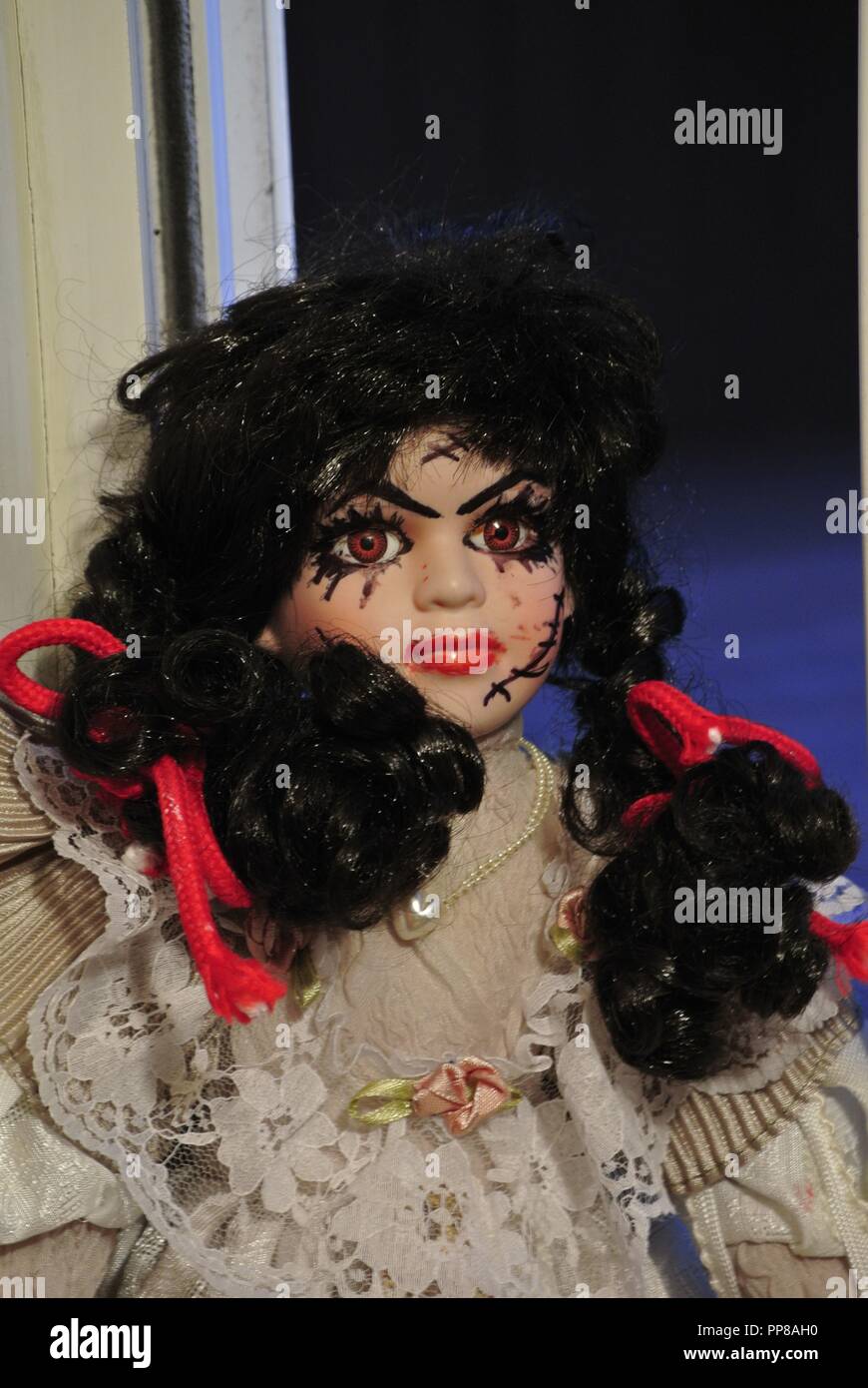 Un primo piano di un antico Bambola porcellana con lunghi capelli neri e un pauroso, bella faccia con cicatrici;, vestito di un bianco Vintage dress, Halloween Foto Stock