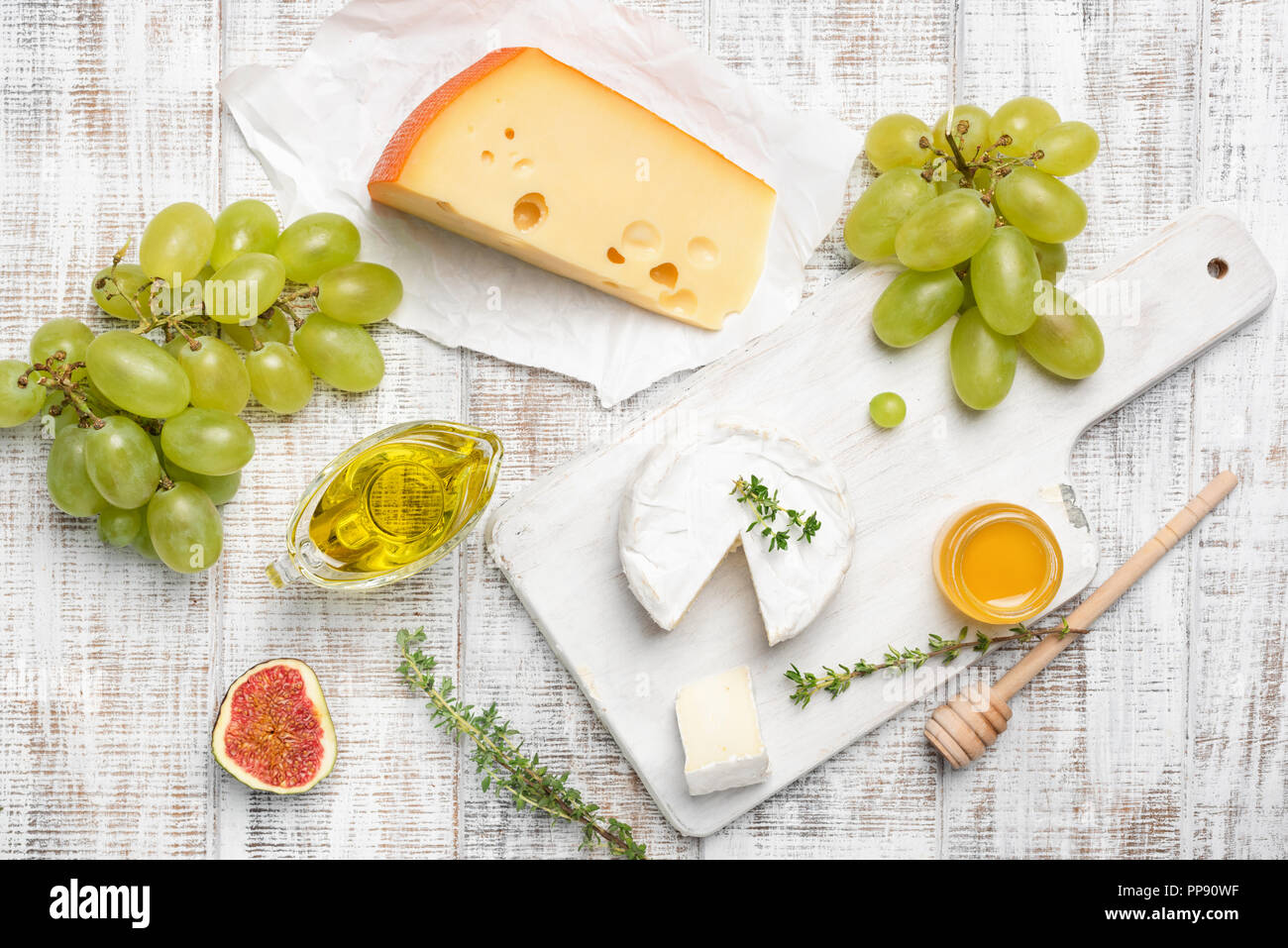 Camembert, giallo formaggio, frutta ed erbe aromatiche in bianco sullo sfondo di legno. Il piatto di formaggi, piatto antipasto. Vista superiore Foto Stock