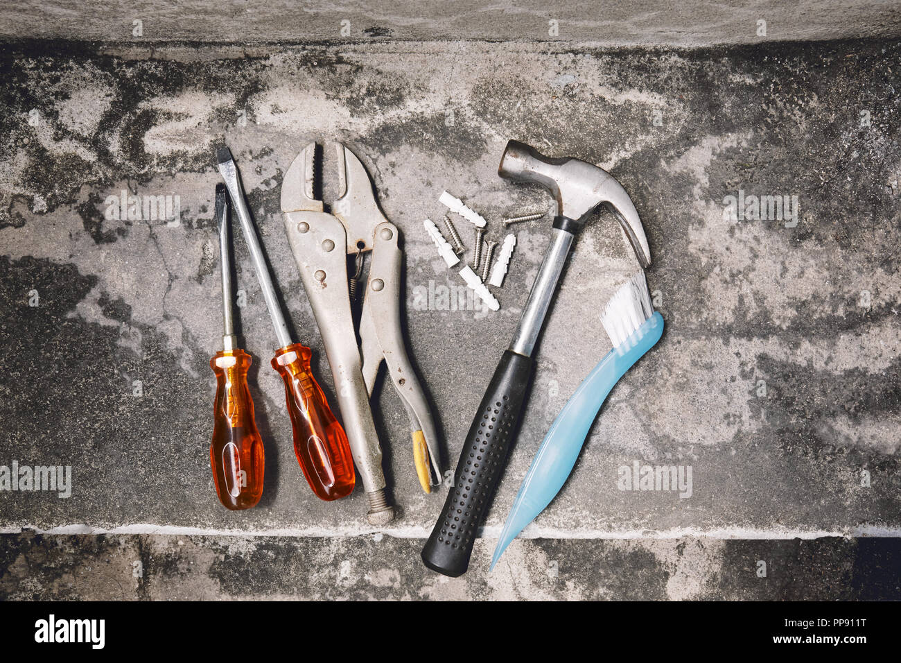 Falegnameria vecchi strumenti di lavoro attrezzature, martello, Chiave, spazzola dura, ancore in plastica e la vite driver sul cemento polveroso, vista dall'alto Foto Stock