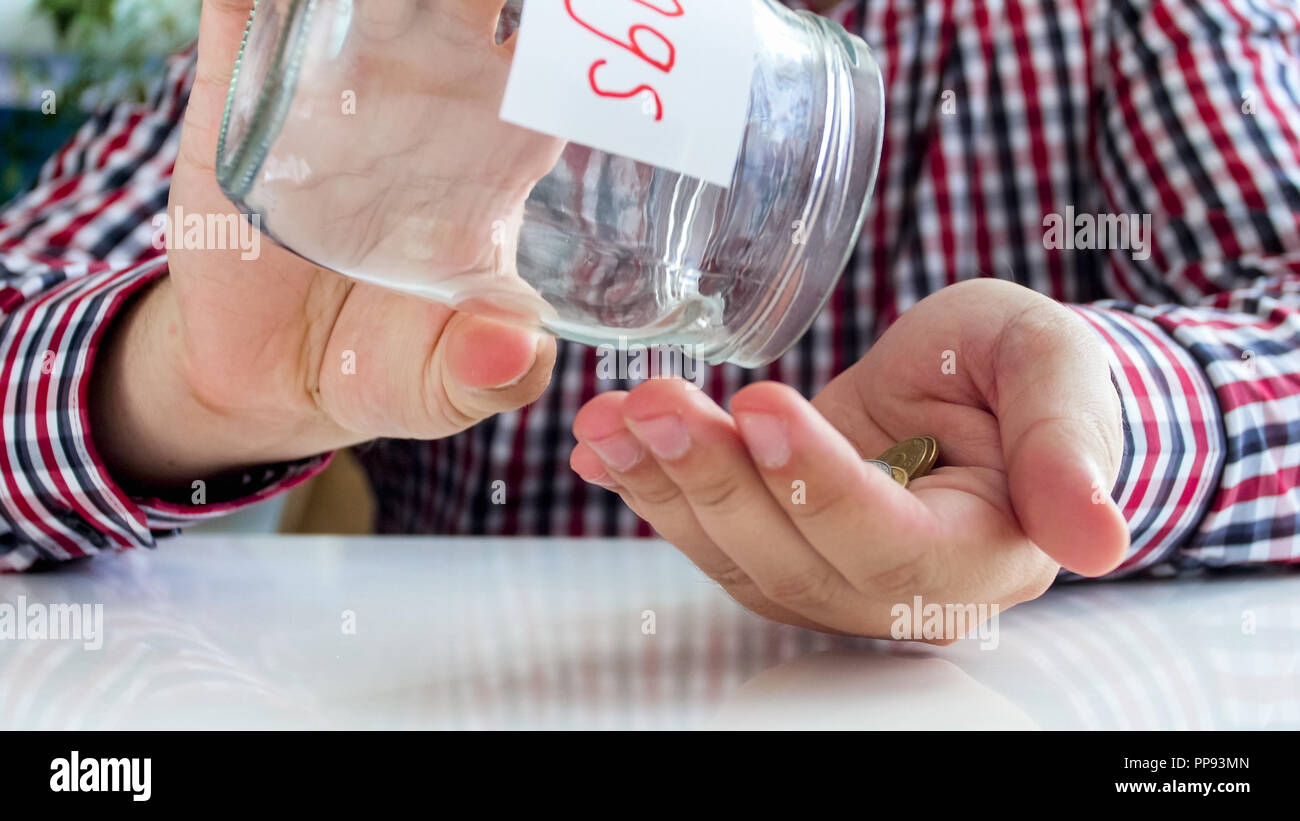 Primo piano immagine della giovane versando poche monete sulle mani per il vasetto di vetro con risparmio di denaro Foto Stock