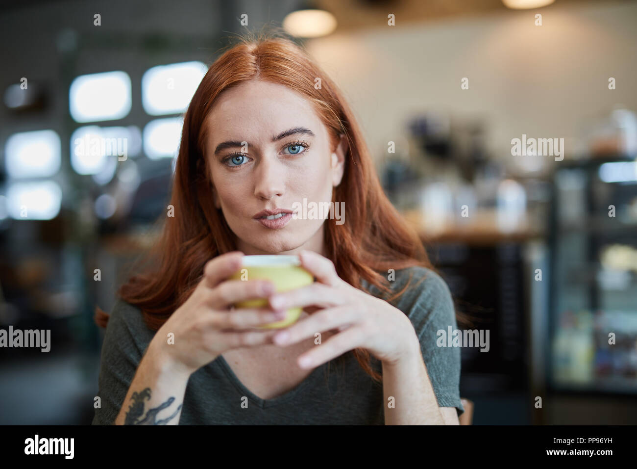 Una singola femmina, si siede in una città cafe tenendo una bevanda calda in una tazza, guardando la fotocamera Foto Stock