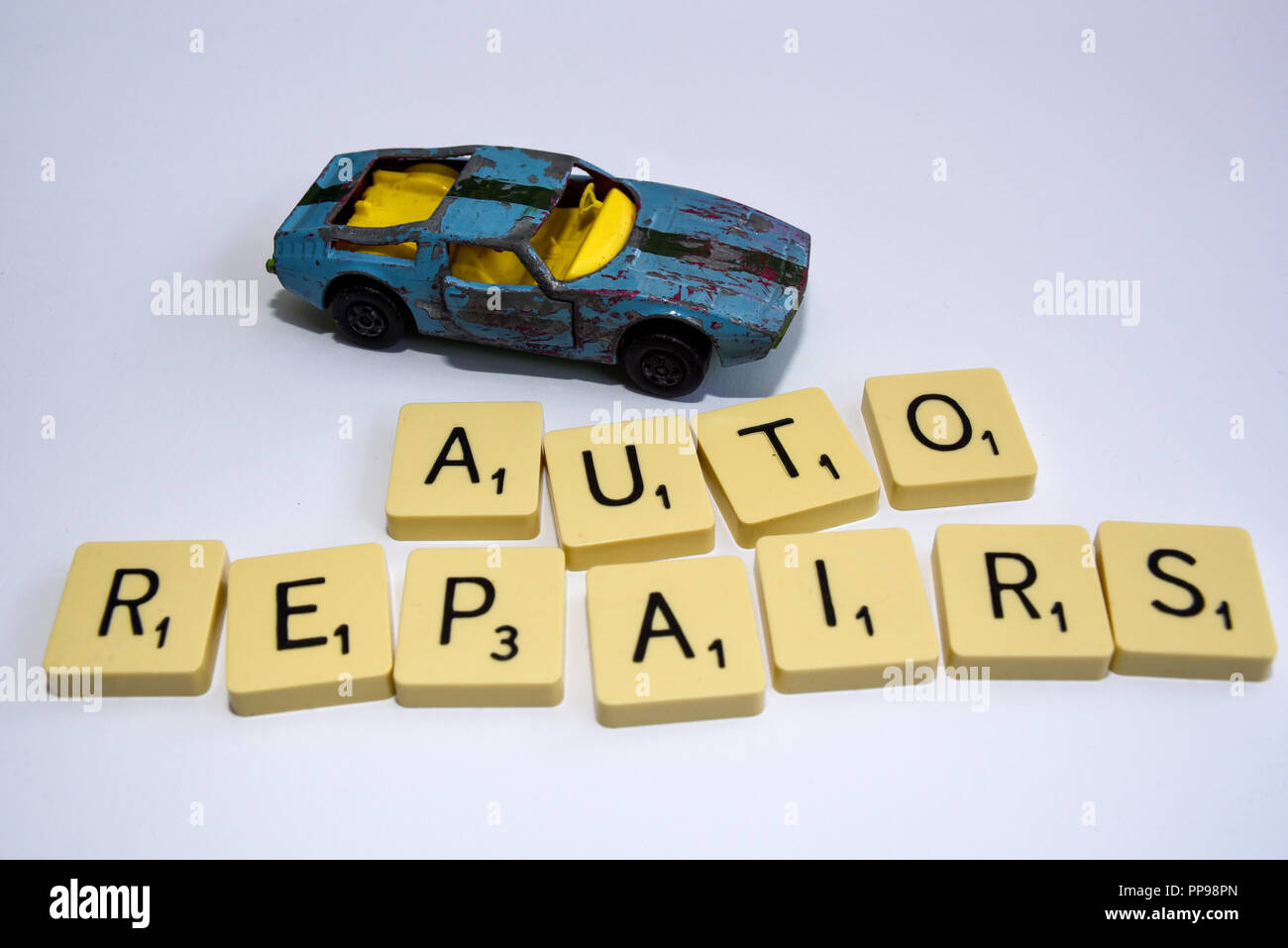 Riparazioni automatiche con il relitto di un'auto giocattolo. Macchinina giocattolo e tessere Scrabble. Riparazioni auto. Garage. Sfondo bianco Foto Stock