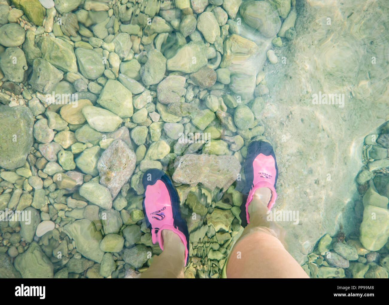 Una donna in piedi in scarpe di immersioni in acque poco profonde sulla spiaggia rocciosa, Ognina, Sicilia Foto Stock