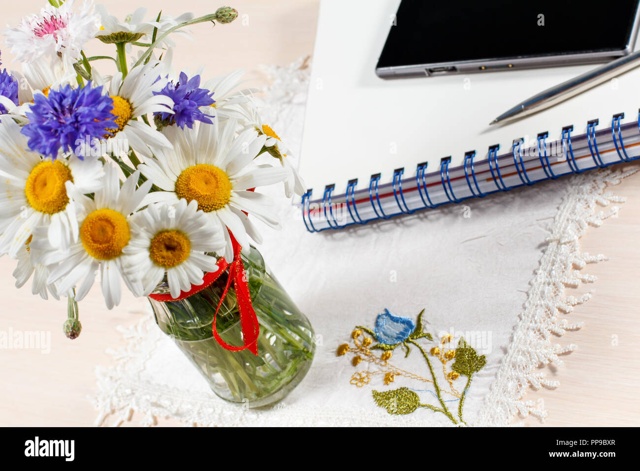 Daisy camomilla e cornflowers in vaso su un tavolo di legno con uno smart-phone, quaderno e una penna Foto Stock