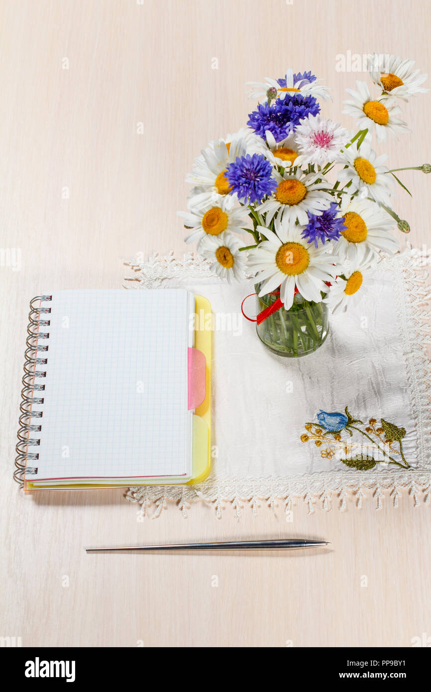 Daisy camomilla e cornflowers in vaso su un tavolo di legno con un notebook e una penna Foto Stock