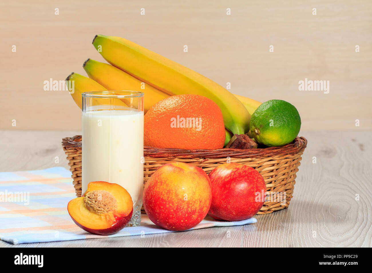 Bicchiere di yogurt deliziosi con la menta e fragole fresche, banana, calce, pesche noci, orange in un cesto di vimini su un tavolo di legno Foto Stock