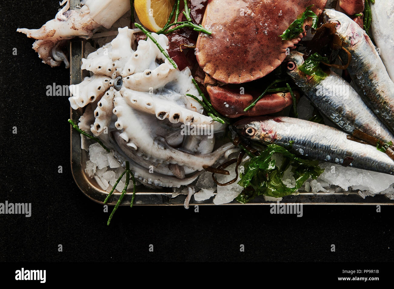 Un piatto di pesce fresco crudo non cotto, tra cui calamari, polpi, sgombro, sardine, ostriche con zampiro e spicchio di limone in vassoio di metallo nero Foto Stock