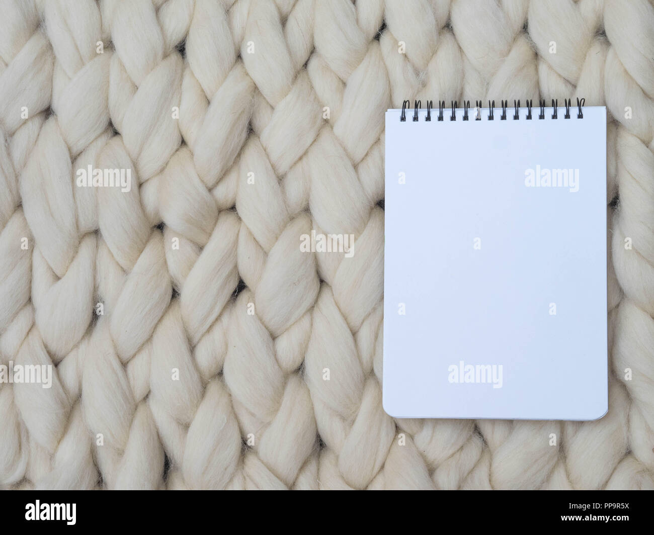 Notebook su lana merinos maglia fatti a mano coperta di grandi dimensioni, super chunky filato, concetto alla moda. Close-up del tessuto lavorato a maglia a una coperta di lana merinos sfondo Foto Stock